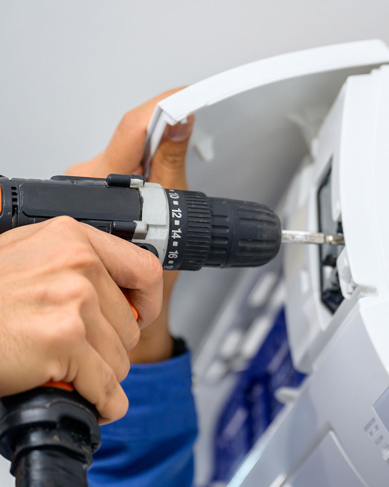 A man repairing an air conditioning unit using a drill
