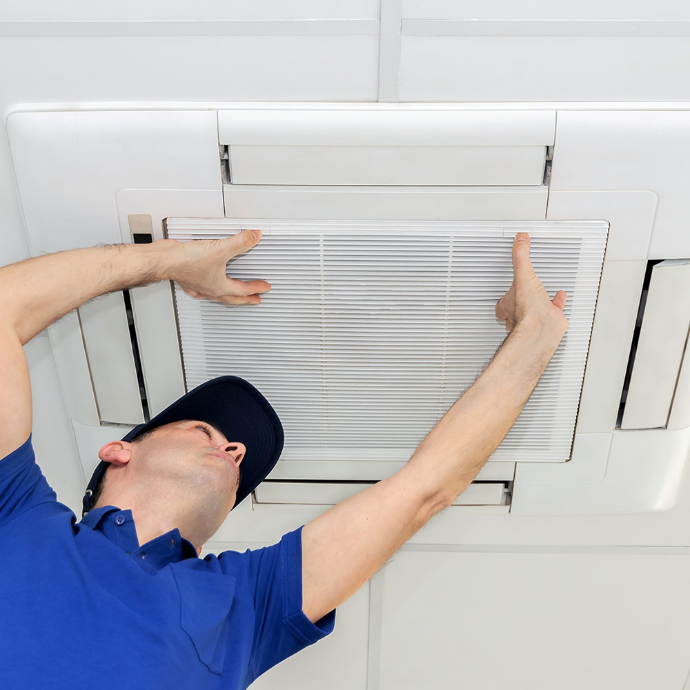 A man in uniform fitting and repairing an air conditioning unit on the ceiling